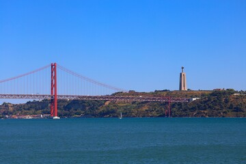 View of famous Lisbon bridge over Tagus river with Jesus Christ statue standing on the hill