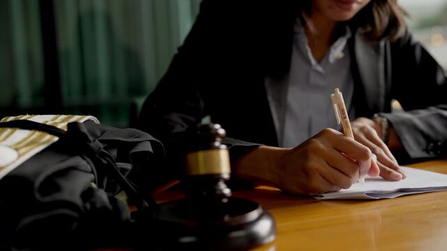 Focused female attorney analyzing court documents at law office desk with gavel and scales.