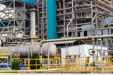 Massive industrial complex shows metal tanks and complex piping with scaffolding and structure.