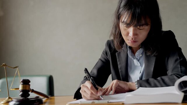 Young female attorney studying legal literature with focus, gavel and scales on table.