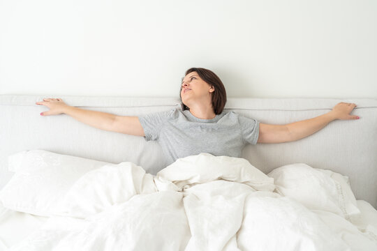 Smiling brunette woman wearing pajama sitting in bed in bedroom