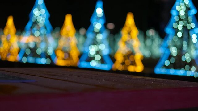 Christmas lights and empty table at night. Blurred christmas trees with blue and yellow lights create a festive backdrop for an empty wooden table at night