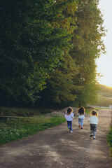 Three children run along a scenic country path at sunset, seen from behind. Happy carefree childhood moments in nature perfect for family, lifestyle, travel, and outdoor concepts. High quality photo