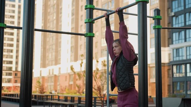 Side view of outdoor trainer gripping pull up bars with hands while lifting legs in urban park workout session, focus on core strength, balance, endurance and technique during body weight exercise