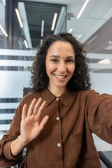 Fotobehang Muziek Young woman with curly hair smiling and waving during a virtual meeting or online conference, communicating remotely from a modern business office environment  © Liubomir
