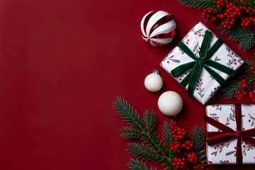 Christmas gifts, ornaments, and red berries on dark red background with copy space.