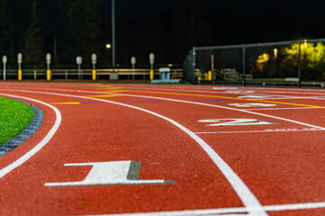 Close up photo of outdoor running track lane white number one, 1, with green shadow, on a new red track with white lane lines.
