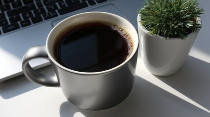 Black coffee in gray mug next to green plant and open laptop on sunny desk