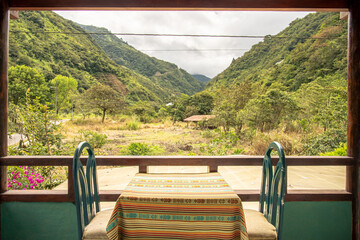 Rustic terrace overlooking lush green Andean mountains in Baños, Ecuador. Serene view with traditional tablecloth and warm natural light.