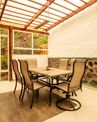 Sunlit rustic dining area featuring stone walls, wooden beams, and a garden view. A peaceful and cozy space that blends nature with simple, timeless design.