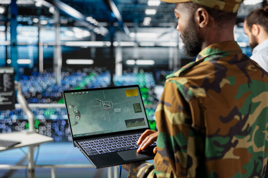 Black military IT expert in server hub using AI tools to oversee battlefield surveillance to develop warfare tactics. Army data center admin doing transmission analysis and live monitoring.