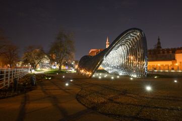 Illuminated stainless steel structure at night on Wyspa Daliowa island in Wroclaw, reflecting city lights. Perfect choice for travel articles, postcards, or city promotion visuals.