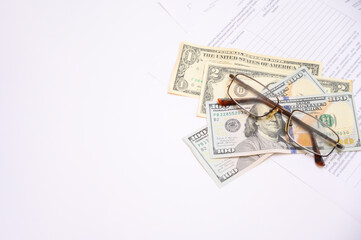 Close-up image showing US dollar banknotes, eyeglasses and financial documents on a white background. Concept of accounting, finance, business analysis, investment and personal budget planning.