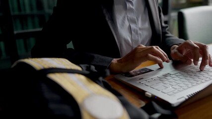 Close-up of hands of young Asian woman in business suit working on laptop, with graduation gown in foreground, symbolizing new graduate starting career or job search. - Powered by Adobe