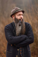 Bearded man with pipe and traditional hat outdoors, rustic lifestyle portrait