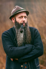 Bearded man with pipe and hat outdoors, rustic Bavarian lifestyle portrait