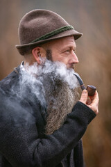 Bearded man smoking pipe outdoors, rustic Bavarian lifestyle portrait in nature