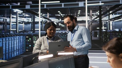 Data center engineering team colleagues collaborating on blade servers maintenance to ensure continuous AI processing. Technicians manage infrastructure supporting machine learning pipelines, camera A