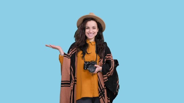 Happy female traveler holding camera, pointing copy space on the blue chroma key