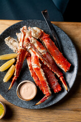 Enjoy succulent crab legs placed on a dark plate, accompanied by tangy lemon wedges and creamy dipping sauce, perfect for seafood lovers seeking a delightful meal