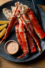 Succulent crab legs are elegantly arranged on a dark plate next to fresh lemon wedges and a small bowl of creamy dipping sauce. A warm, inviting atmosphere enhances the dining experience