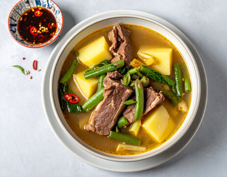 Savory Filipino Beef Nilaga - A Hearty Stew of Tender Meat, Potatoes, and Green Beans in a Golden Broth, Viewed from Above.