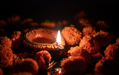 Closeup of Diwali Diya or Clay Oil Lamp with  Marigold Flowers and Glowing Flame with Selective Focus and Copy Space, Happy Diwali or Deepavali Celebration Conceptual, Festival of Lights