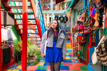 Happy young Latina woman in vibrant outfit enjoys a walk through colorful artisan stores in Caminito, Buenos Aires, Argentina. Famous spot in La Boca full of art and life © Itza
