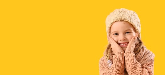 Happy little girl in winter clothes on yellow background with space for text