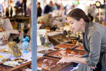 Cheerful female tourist choosing antique jewelry at flea market