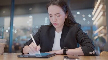 Asian businesswoman writing on digital tablet while checking phone at cafe. Concept of high-efficiency workflow, smart workspace and multitasking leader. - Powered by Adobe