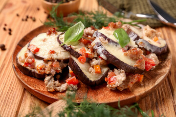 Plate with baked eggplant slices, ground meat, vegetables, cheese and dill on wooden background