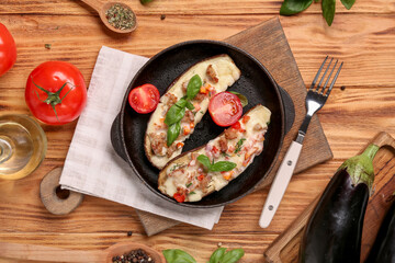 Baking dish with stuffed eggplants, tomatoes and basil leaves on wooden background