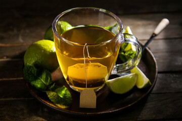 Cup of hot tea with limes and mint leaves on dark wooden background