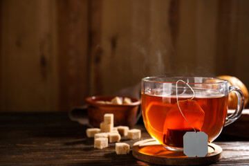 Cup of hot tea with sugar cubes on wooden background