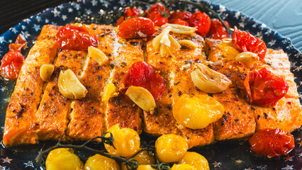 Beautifully baked salmon fillet with roasted garlic, caramelized yellow and red cherry tomatoes, and fresh herbs, served hot on a plate. A delicious and healthy gourmet meal.