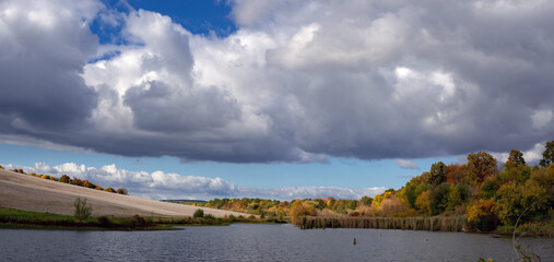 Recreation area by a pond. Early autumn by a quiet lake. Panoramic view of an autumn landscape near a rural pond. A mesmerizing autumn scene.