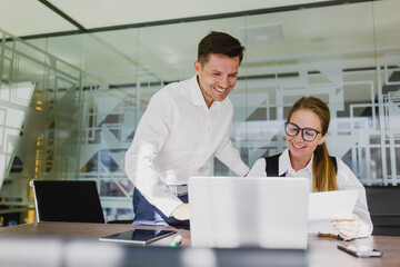 Business professionals collaborate on a project in a modern office setting, discussing ideas while using a laptop and printed materials