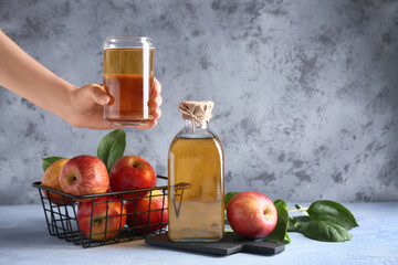 Female hand with fresh fruits, bottle and glass of apple cider on grey grunge background