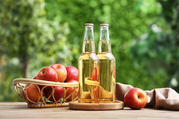 Fresh fruits with bottles of apple cider on wooden table outdoors
