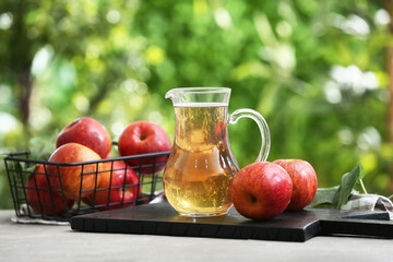 Fresh fruits and jug of apple cider on grey table outdoors