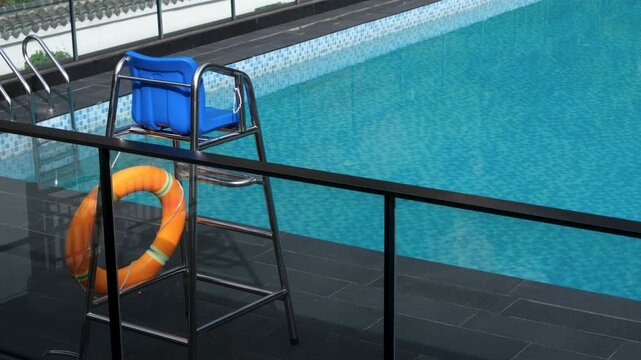 a lifeguard chair and safety ring or lifebuoy beside the clear blue water of an empty swimming pool. Modern poolside design with public or community safety features in a leisure facility environment.