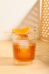 Glass of tasty Old Fashioned Cocktail with orange slice on wooden table against light wall