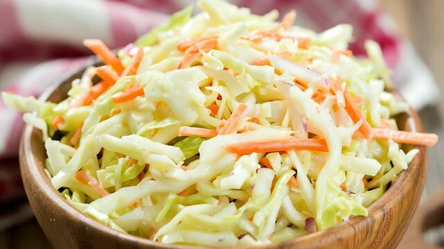 This is a close-up  of a dish filled with crunchy shredded cabbage and carrots, served in a wooden bowl. The vegetables are drenched in a creamy dressing, giving it an appetizing look.