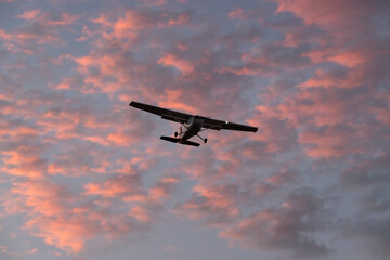 Small Aircraft Flying at Sunset with Colorful Clouds