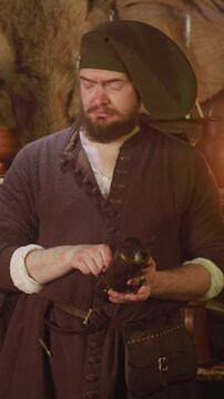 Merchant checks roots in capsule in store. Serious bartender in medieval dress takes potion ingredients out of decorative container in tavern. Seller goods