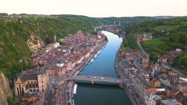 citadel church meuse river flowing below mountains above traffic bridge boats evening light green fields beyond dinant belgium left pull pullback drone shot 