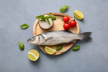 Wooden plate with fresh raw seabass fish and different ingredients on blue background