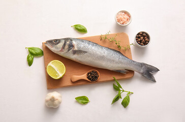 Wooden board with fresh raw seabass fish and different spices on white background
