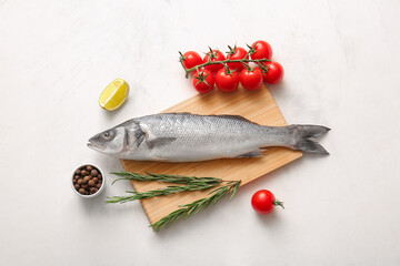 Wooden board with fresh raw seabass fish and different ingredients on white background